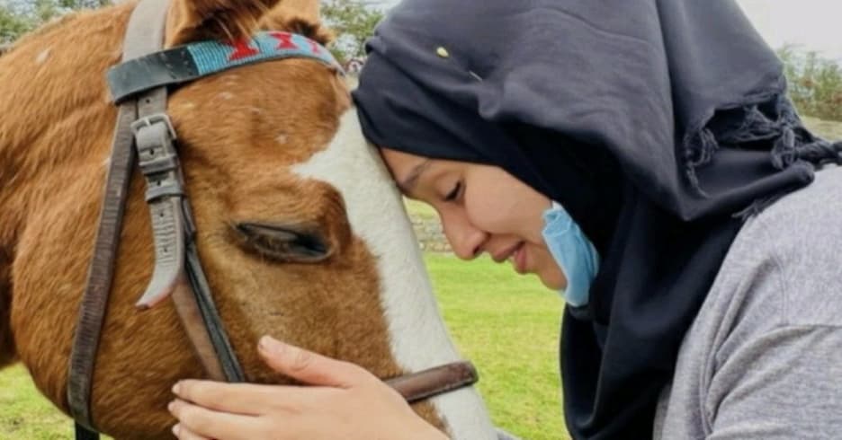 A person holding their head to a horse