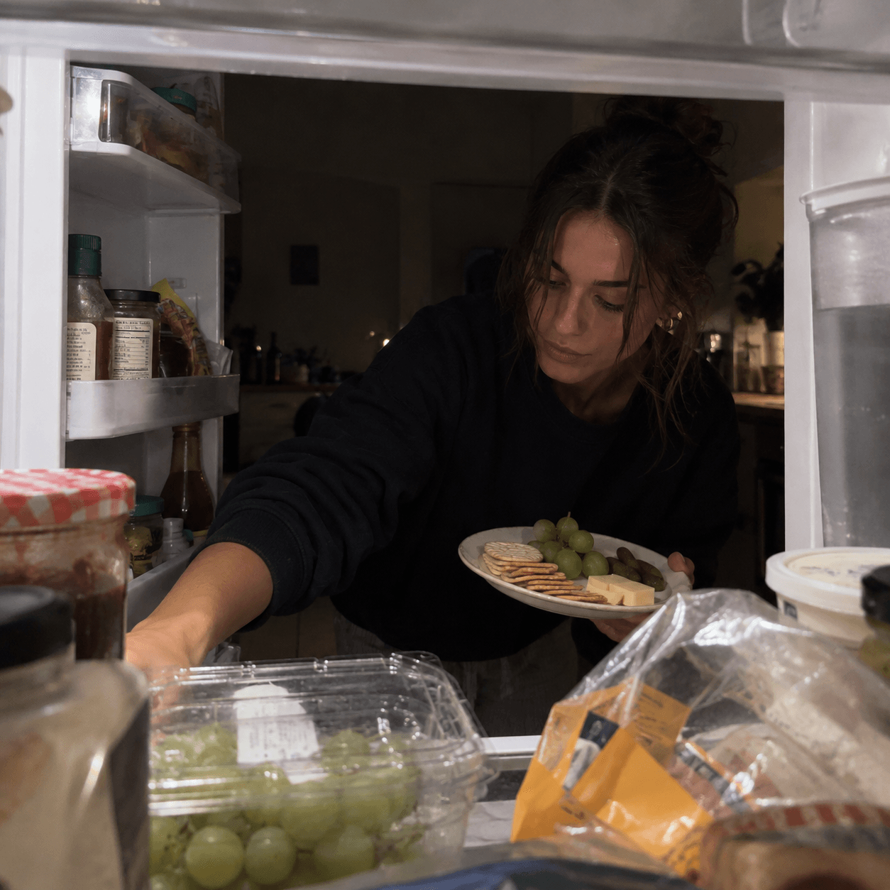 A woman looking through her fridge finding things to eat. The perfect example of girl dinner.