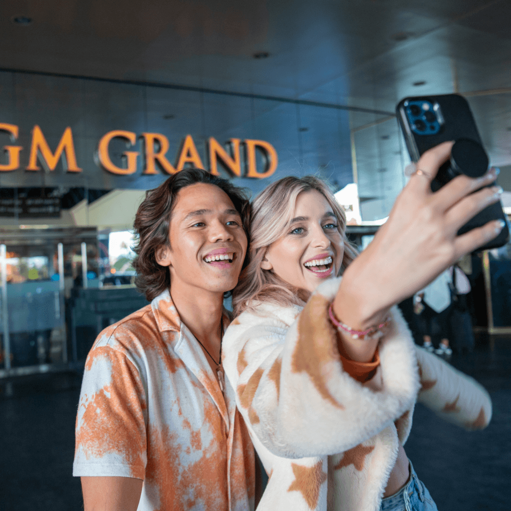Two people taking a selfie in front of a MGM Grand building