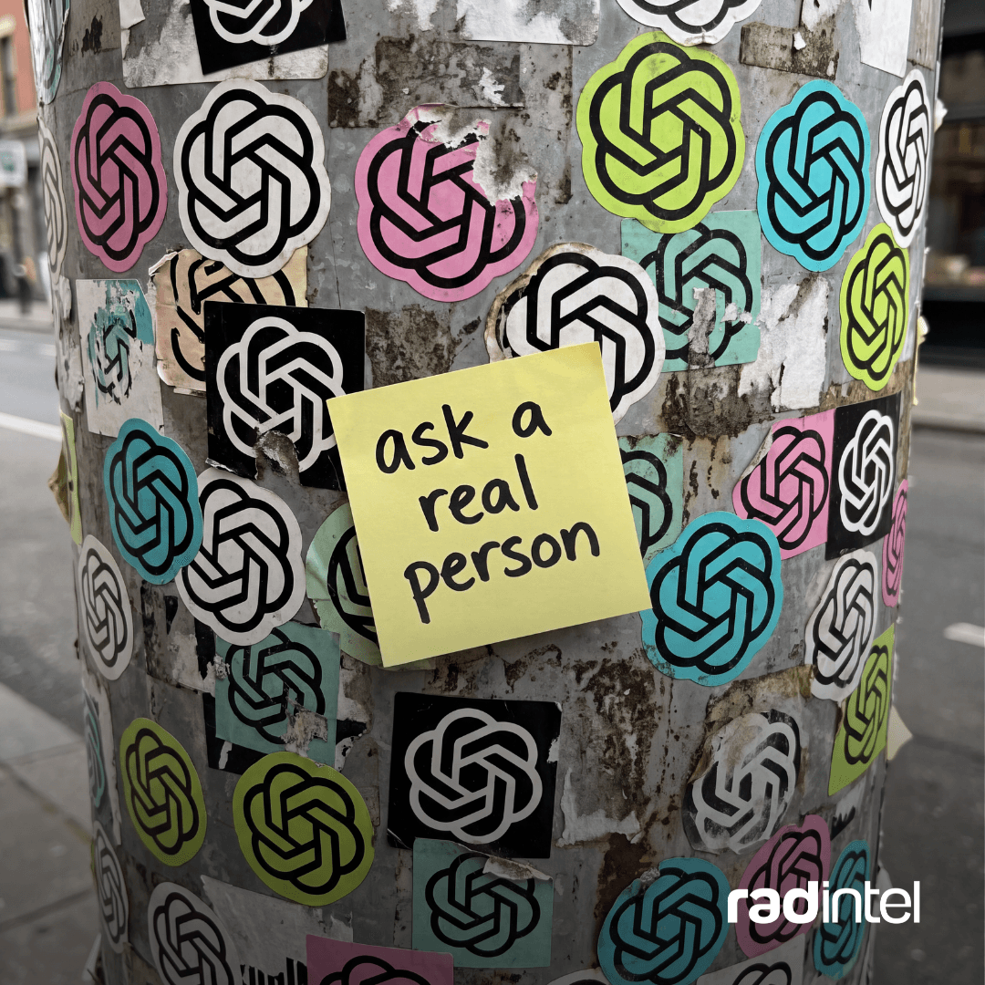 A street pole covered in colorful OpenAI logo stickers, with a single yellow sticky note in the middle that reads “ask a trusted source.”